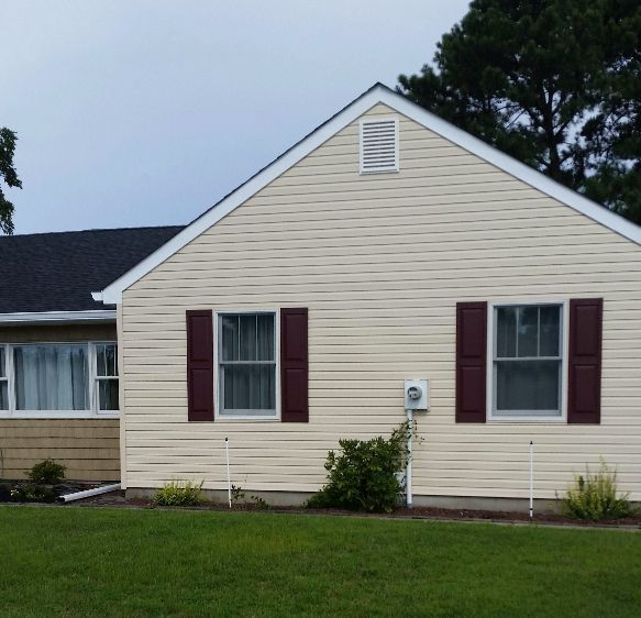 Beige house with burgundy shutters, dark roof, and green lawn.