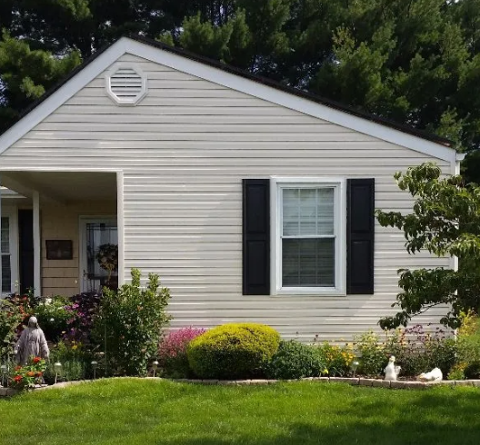 Beige house with black shutters, green lawn, and garden.