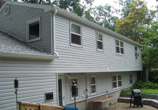 Two-story house with gray siding, several windows, and a backyard with a barbecue grill.