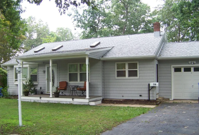 Gray bungalow with a porch, garage, and green lawn.
