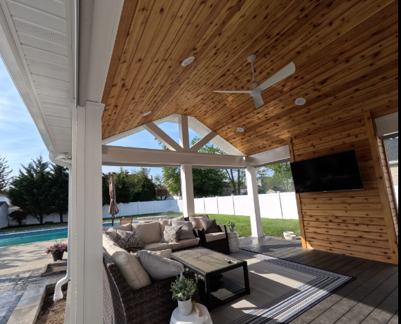 Covered patio with cedar ceiling, white columns, outdoor furniture, and a pool in the background.