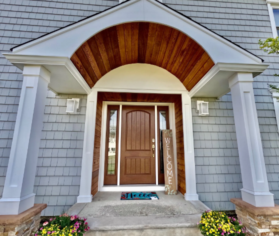 A front door with a wooden door, topped with an arched awning, flanked by white pillars, and gray siding.