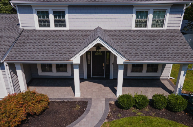 Gray house with white trim, front porch, and black door, featuring landscaping.
