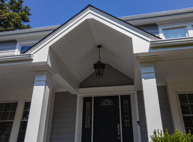 White-pillared porch entrance with a black door, gray siding, and a hanging light fixture.