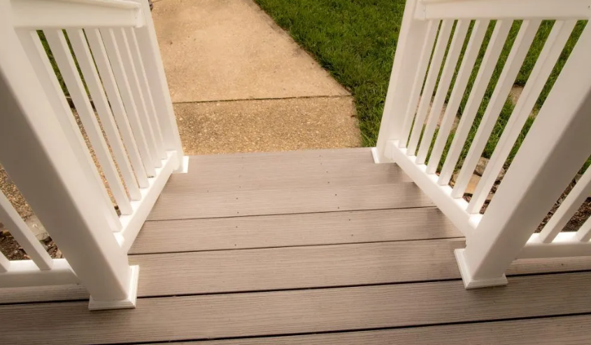White railing frames wooden steps leading to a concrete walkway and green grass.