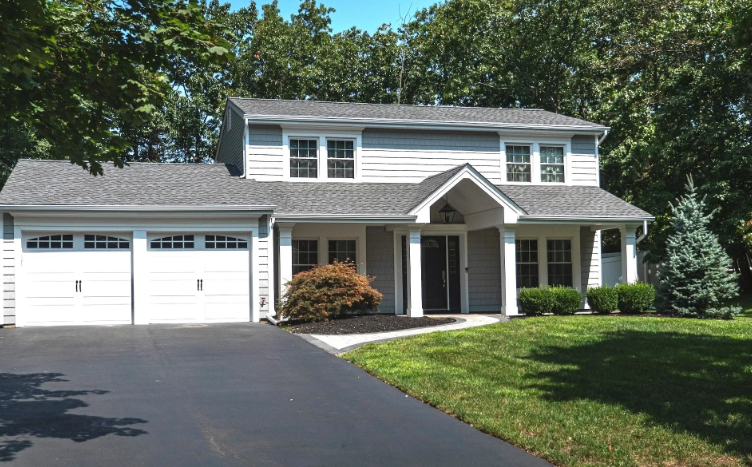 Two-story gray house with white trim, a black driveway, and a well-manicured lawn on a sunny day.
