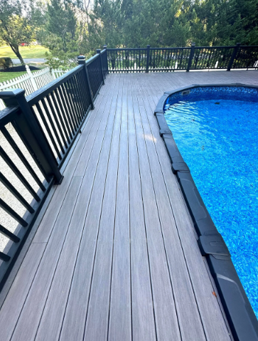 Gray composite deck surrounds a blue pool, with black railing and trees in the background.