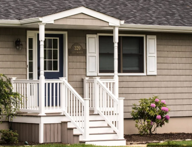Beige house with blue door and white porch, steps, and shutters; pink bush.