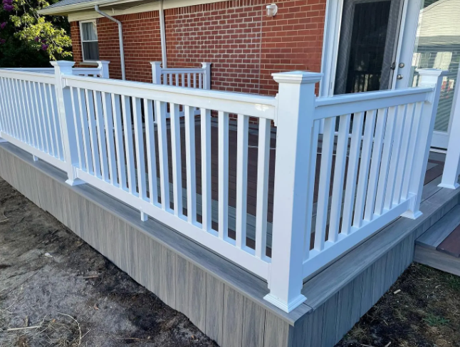 White railing on a deck with grey composite skirting against a brick house.