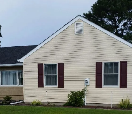 Tan house with burgundy shutters, dark roof, and small ventilation opening.