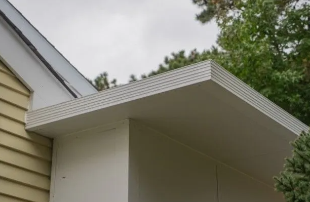White soffit and trim on a building with yellow siding; cloudy sky and trees visible.