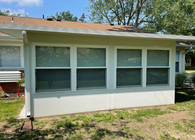 Sunroom addition with white walls, four windows, and a brown roof.