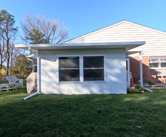 White-walled addition on a house with two windows, attached to a brick section. Green lawn and blue sky.