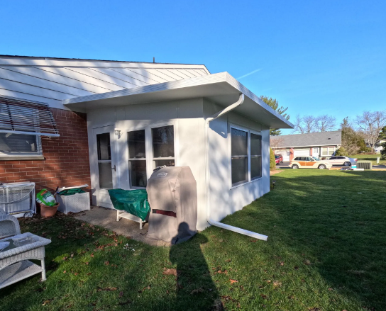 White stucco sunroom addition with windows, attached to a brick house with a green lawn.