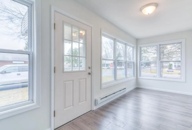 Sunroom with door and windows, hardwood floors, white walls, and a light fixture.