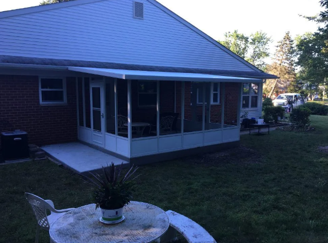 Screened-in porch on a brick house; white roof, concrete patio, a table with plant, green yard.