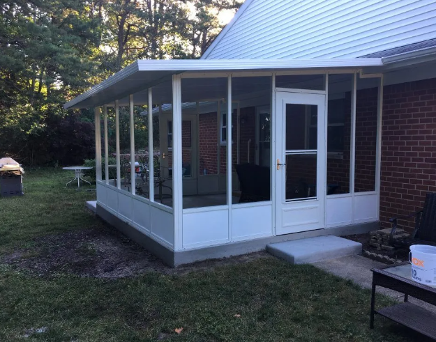 White-framed screened porch attached to a brick house, with a door and concrete steps.