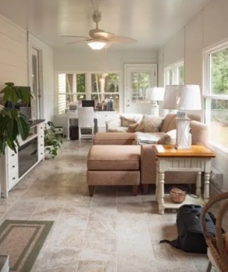 Sunroom with neutral-toned furniture, ceiling fan, windows, and plants.  A work desk sits near a bank of windows.