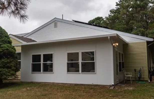 White sunroom attached to a yellow house with windows, set in a yard under a cloudy sky.