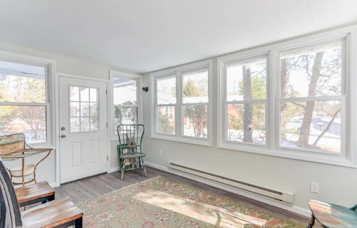 Sunroom with white trim and numerous windows, door. Green chair, wood floor.