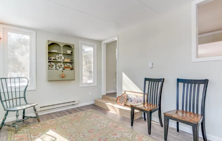 Interior room with two black chairs, one green chair, a rug, and a cabinet with plates.