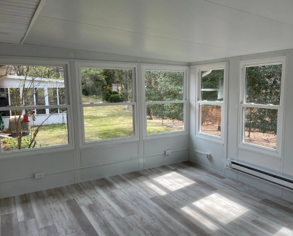 Sunroom with light gray wood-look flooring, white walls, and multiple windows overlooking a grassy yard.