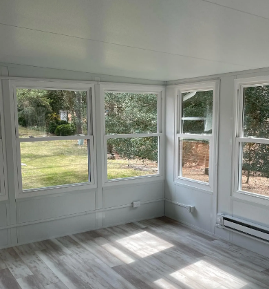 Sunroom with multiple windows overlooking a yard; white walls and ceiling; laminate floor.