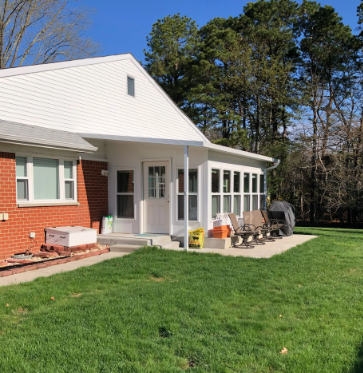 White sunroom addition on a brick house with a green lawn and trees in the background.