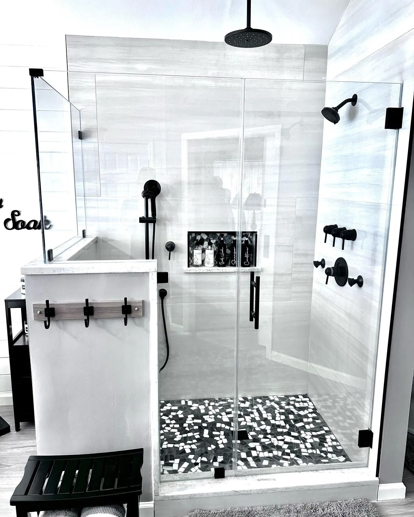 Modern bathroom with glass shower enclosure, black fixtures, and mosaic floor.