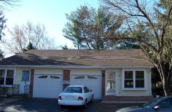 Two attached houses, yellow siding, brown roof, white garage doors, a car parked in front.