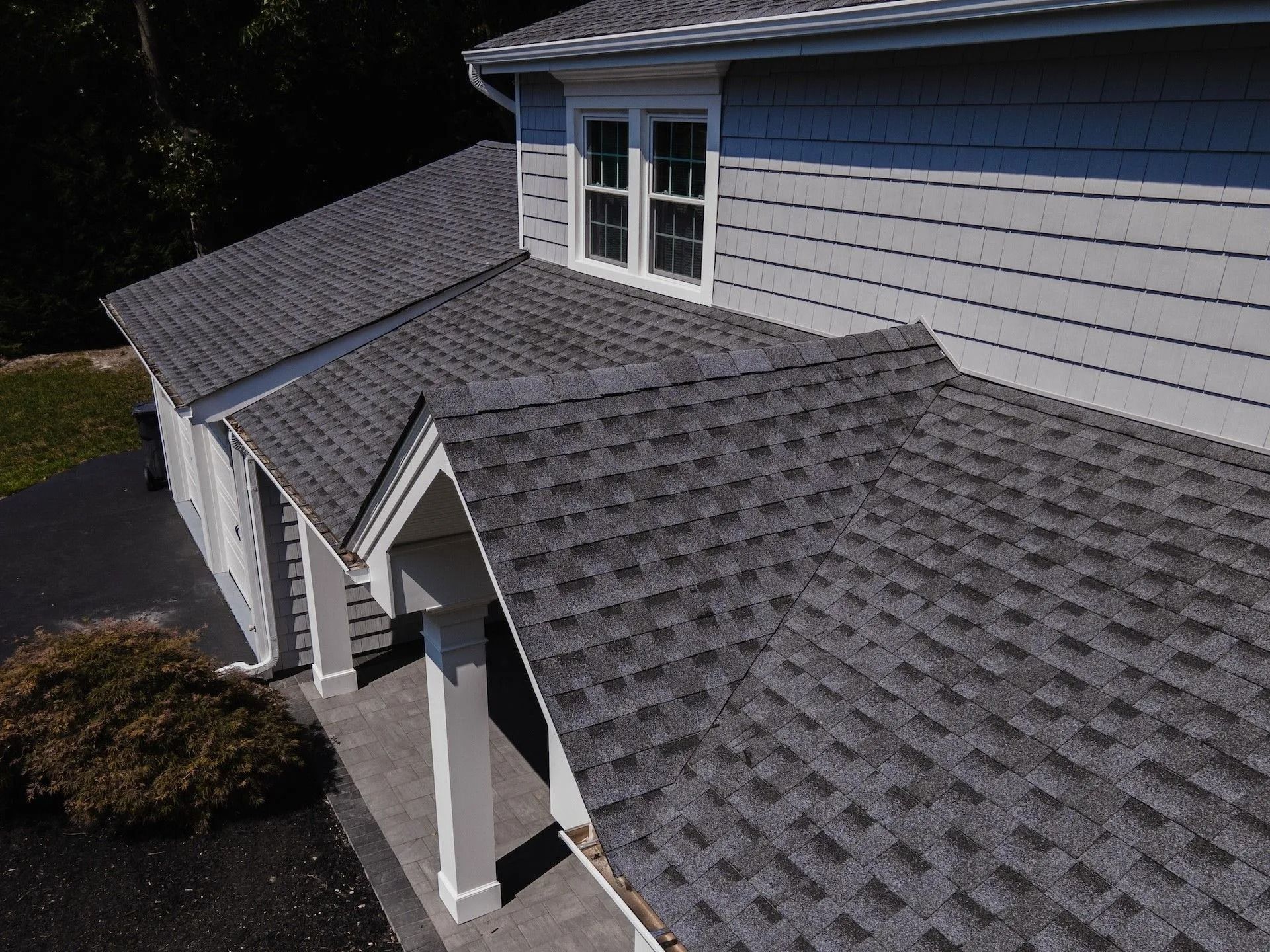 Gray asphalt shingle roof on a house with gray siding. Sunlight highlights the roofing material.