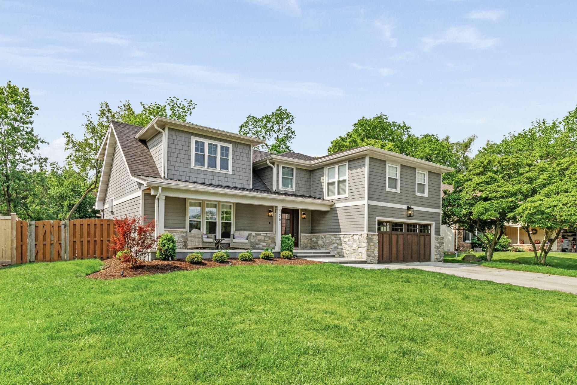 Gray two-story house with green lawn, wooden garage door, and a covered porch.