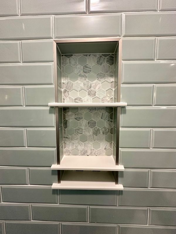 Bathroom shower tile niche with two shelves, grey subway tiles, and hexagon tile backing.