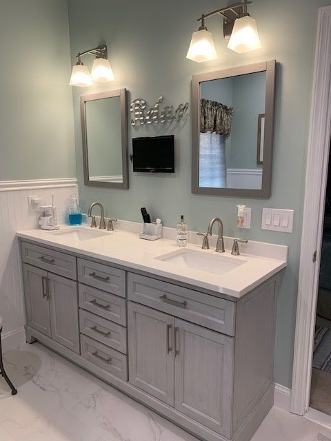 A bathroom with a double sink vanity, mirrors, and sconce lighting against a light blue wall.
