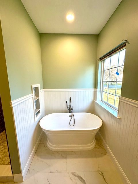 A small bathroom with a freestanding white bathtub, green walls, and a window.