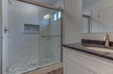 Bathroom with marble-like shower, glass door, and white vanity with dark countertop.
