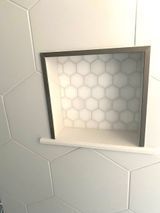 Recessed shower shelf with honeycomb tile back and gray trim.