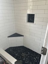 White-tiled shower with black pebble floor, corner bench, and recessed shelf.