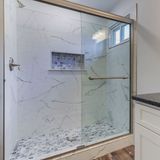 A marble-tiled shower with a glass door and a small niche.