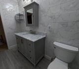 Gray bathroom with vanity, toilet, and marble-look tiled walls.