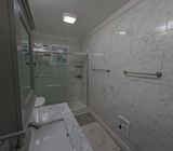 Bathroom with marble-look tile walls, glass shower, vanity sink, and silver fixtures.