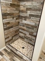 Shower with wood-look tile walls, pebble floor, and dark frame.