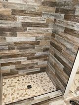 Shower with wood-look tile walls, pebble tile floor, and a dark drain.