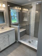 Bathroom with a white vanity, a glass shower with a built-in bench, and gray tile.