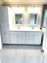 White double bathroom vanity with mirrors, lights, and storage cabinet. Gray tile floor.