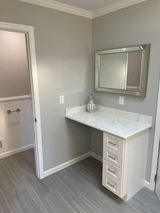 Bathroom vanity with marble countertop, mirror, and drawers, next to an open doorway. Gray walls and flooring.