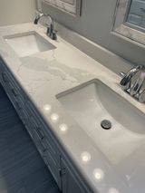 White quartz countertop with two sinks, chrome faucets, and a cabinet base.