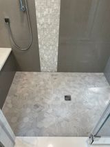 Bathroom shower with gray and white tile, shower head, bench and drain.