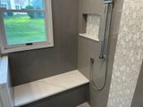 Gray-tiled shower with a white bench and niche. A window is on the left.