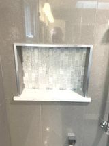 Recessed shower niche with mosaic tile backing, surrounded by a metal frame and light gray tile.